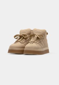Sneaker alte beige con punte arrotondate, colli imbottiti, lacci in raso e suola spessa in gomma. Presentano tre righe laterali e un accento con logo.