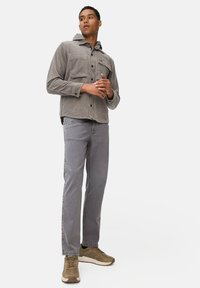 Chemise en velours côtelé grise avec capuche, deux poches poitrine et manches longues. Associée à un jean gris clair et des baskets olive.
