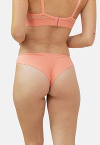 Bas de bikini rose corail avec une texture lisse et une coupe basse, présentant un subtil éclat et des lignes nettes. Aucun motif ou matériel visible.