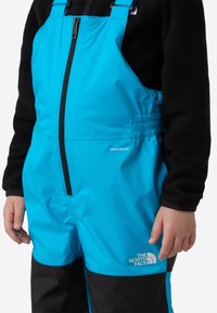 Blue waterproof overalls feature a black panel at the bottom, zip front, adjustable straps, and "DRYVENT" branding on the chest.