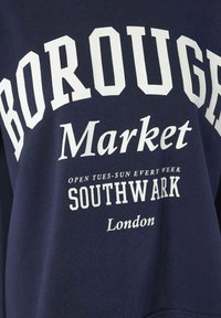 Tamsiai mėlynas audinys su baltu tekstu, skaitant: Borough Market, atidarytas antradieniais-šeštadieniais kiekvieną savaitę, Southwark, Londonas.