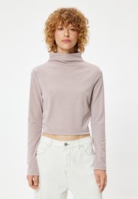 Lichtroze, cropped langskap turtleneck-top met een zachte textuur en subtiele ribbelpatroon, gecombineerd met witte high-waist jeans.