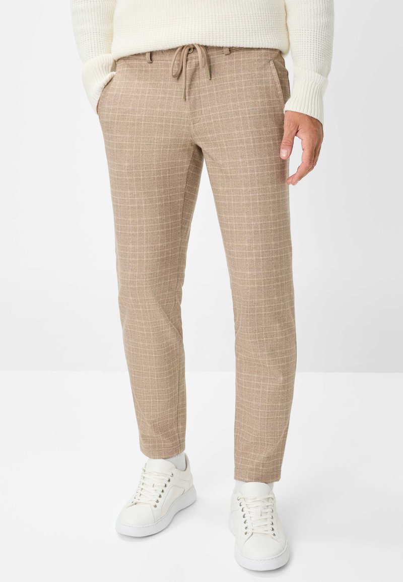 Beige geblokte broek met een relaxte pasvorm, een tailleband met trekkoord, zijzakken en een enkelvoudige zoom, gecombineerd met witte sneakers.
