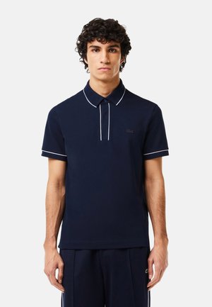 Marineblauwe polo met een slim fit, contrasterende witte kraag en mouwstrepen, en een klein geborduurd logo op de borst.