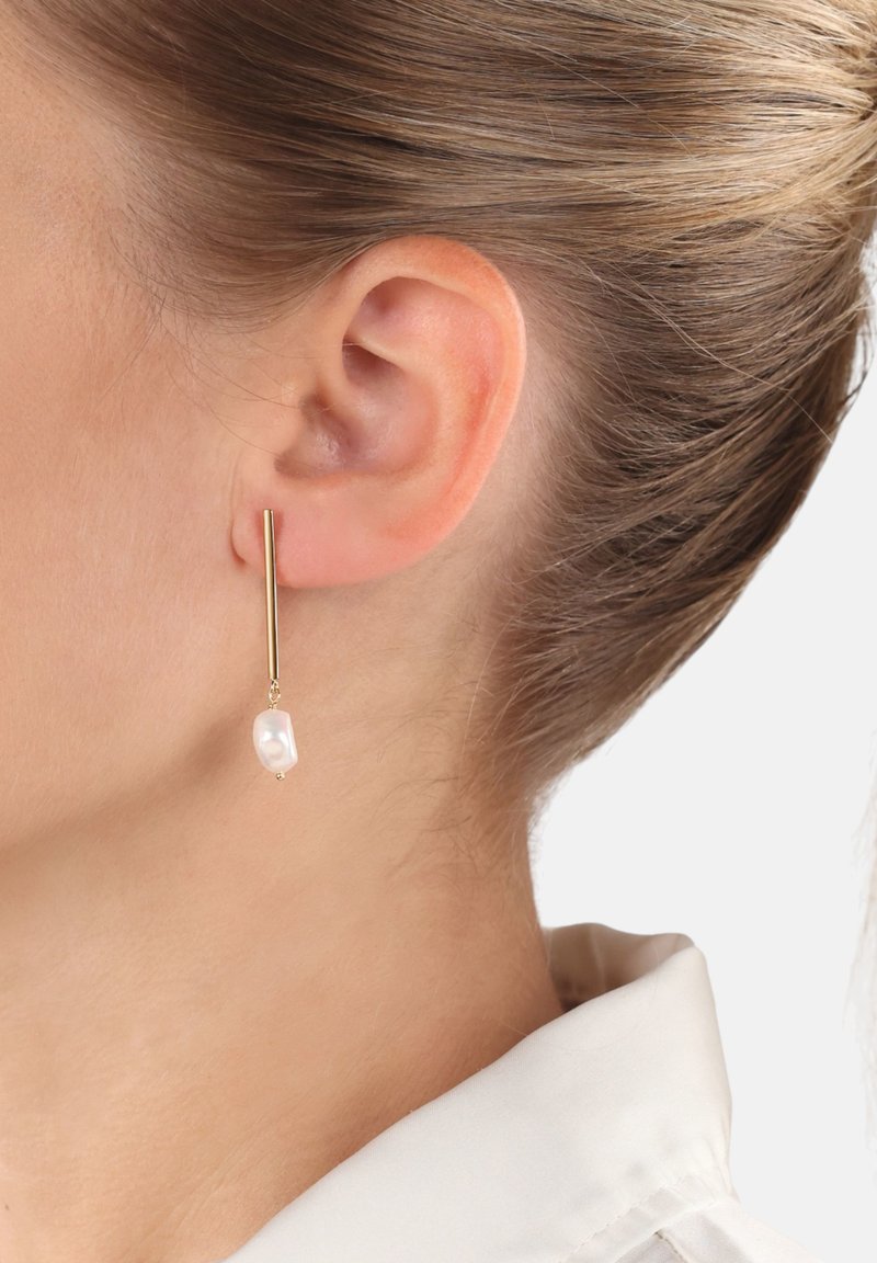 Orecchini in oro con un design a barra lunga e sottile, caratterizzati da un'unica goccia di perla bianca irregolare che pende elegantemente vicino al lobo dell'orecchio.