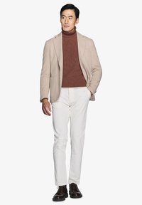Beige blazer over en brun turtleneck, matchende med hvide corduroypants og mørkebrune sko. Glat stof og skræddersyet pasform.