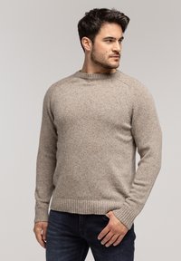 Beżowy sweter dzianinowy z okrągłym dekoltem, ściągaczami na mankietach i u dołu. Teksturowany materiał ma subtelne kropek i luźny fason.