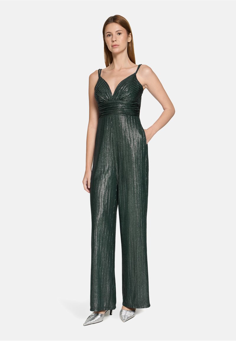 Combinaison métallique verte avec un profond décolleté en V, un corsage plissé et des jambes larges. Caractérisée par des bretelles fines et deux poches latérales. Escarpins argentés.
