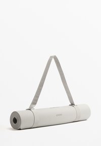 Siva jogijska podloga zvita, z teksturirano površino in blago trak za enostavno nošenje. Na podlogi je jasno vidno ime blagovne znamke "OYSHO".