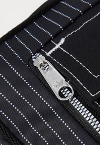Borsa in tessuto nera con strisce verticali bianche e pois blu. Presenta una cerniera argentata con il logo Adidas e un tirante testurizzato.