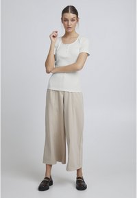 Hvid ribbet kortærmet top med rund halsudskæring og knapdetaljer, parret med beige brede bukser og mørke loafers.
