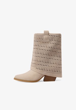 Botín beige de ante con patrones circulares y triangulares cortados con láser, tacón de bloque de madera inclinado y lengüeta en el puño.