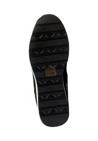 Semelle de chaussure noire avec des motifs de crampons, des rainures horizontales, et une petite étiquette affichant des symboles d'entretien et du texte près du centre.