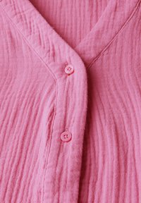 Chemise en coton rose avec une texture côtelée, un design en V et deux boutons assortis rose. Tissu doux et léger avec des lignes subtiles.