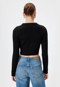 Zwarte geribbelde gebreide cropped trui met lange mouwen, gecombineerd met lichtblauwe high-waisted denim jeans met een leren merklabel.
