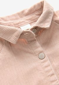 Camisa de pana de color rosa claro con cuello y cierre de botones, que presenta una sutil textura de rayas verticales. Etiqueta visible cerca del cuello.