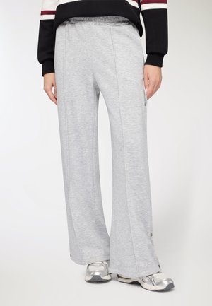 I pantaloni della tuta grigi chiaro a gamba larga presentano una vita elasticizzata e dettagli con bottoni a pressione lungo i lati. Il tessuto è morbido e liscio.