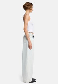 Hellblaue weite Jeans mit hoher Taille, die einen ausgewaschenen Look und kontrastierende Nähte aufweisen, kombiniert mit einem weißen Tanktop.