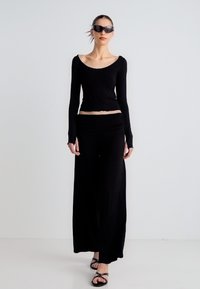 Μαύρο τοπ με μακριά μανίκια και φούστα με ρέον ύφασμα, ελαφρύ, με εφαρμοστή μέση και χαλαρή σιλουέτα, συνδυασμένα με σανδάλια με λουράκια.