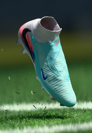 Nike soccer cleat featuring a turquoise and white knitted upper, a snug ankle collar, and a colorful gradient sole. Silver cleats accent the bottom.