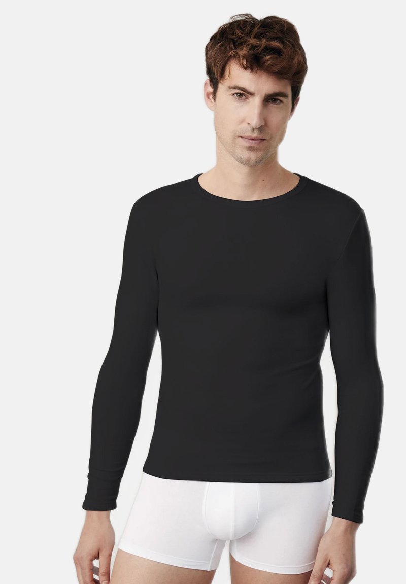 Camisa negra de manga larga hecha de una tela suave, con un escote redondo. Llevada con ropa interior blanca ajustada.