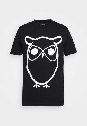 T-shirt di cotone nero con una grande grafica di un gufo bianco, caratterizzato da occhi circolari e linee semplici, maniche corte e colletto a girocollo.
