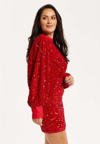 Red sequined mini dress with puffed sleeves and a solid red cuff. The dress features a tight fit and a textured, shiny surface.