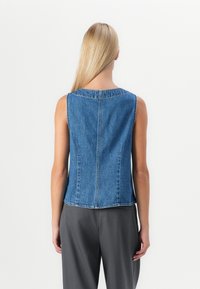 Denim mouwloos topje met een boxy ontwerp, ronde hals en een naad in het midden van de rug. De stof heeft een robuuste textuur; de kleur is middelblauw.