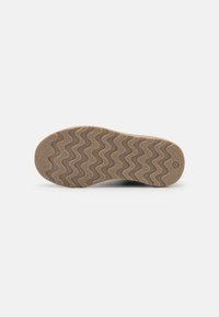 Semelle d'une chaussure avec un motif de semelle ondulé, fabriquée en caoutchouc texturé, de couleur beige pâle, avec un logo de marque circulaire et une indication de taille.