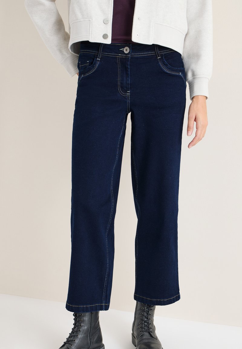 Navyblauwe cropped jeans van denim materiaal met contrasterende stiksels, een vijf-pocket ontwerp en een sluiting met een knoop aan de voorkant. G gedragen met zwarte laarzen.