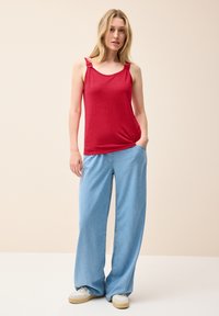 Top sin mangas rojo con tirantes con volantes, combinado con pantalones de mezclilla ligeros de corte holgado en azul claro y zapatillas blancas, sobre un fondo neutro.