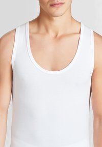 Canotta bianca senza maniche in cotone. Presenta un collo rotondo e una silhouette liscia, leggermente aderente. Nessun motivo o accentuazione visibile.