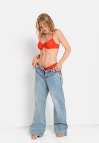 Haut de bikini rouge avec un nœud à l'avant, associé à un jean en denim bleu clair surdimensionné. Tissu doux, coupe décontractée, design à jambes larges.