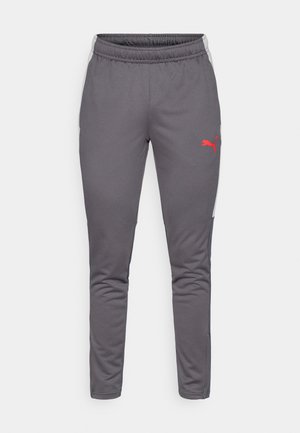 Pantaloni atletici gri cu croială conică, talie elastică, buzunare laterale și un logo Puma roșu; prezintă un material texturat și accente laterale moi contrastante.