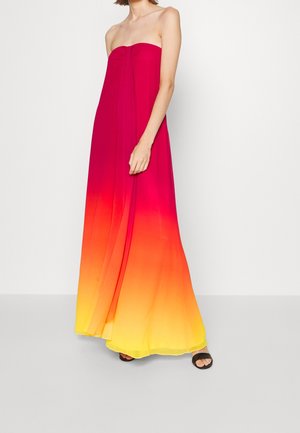 Robe maxi bustier avec des couleurs dégradées passant du rouge en haut à l'orange et au jaune en bas, portée avec des sandales noires à bout ouvert.