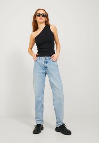 Top senza maniche nero a spalla unica, jeans azzurri dalla vestibilità comoda, scarpe nere con lacci. Tessuto morbido, design minimalista, estetica casual.