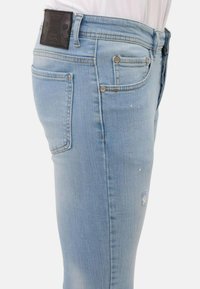 Lichtblauwe denim jeans met een slim fit, gekenmerkt door een vervaagde textuur, versleten details en een zwart merklabel op de tailleband.