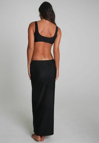 Schwarzes Zweiteiler-Outfit bestehend aus einem taillierten Bralette und einem langen, fließenden Rock. Glatter Stoff mit minimalen Nähten, der eine elegante Silhouette betont.