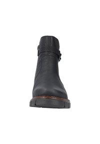 Bottine en cuir noir avec un bout arrondi, dotée d'une sangle texturée, d'une boucle sur le côté et d'une semelle en caoutchouc avec un léger talon.
