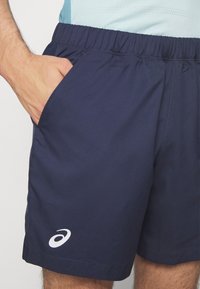 Pantalones cortos deportivos azul marino hechos de una tela ligera, con una cinturilla elástica, bolsillos laterales y un logo blanco en la parte inferior de la pierna izquierda.