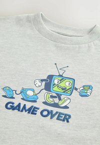 Harmaa villapaita, jossa on piirretty hahmo, joka muistuttaa televisiota vihreällä naamalla, pitäen peliohjaimia kädessään, ja "GAME OVER" kirjailtuna sinisellä.