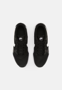 Nike Air kengät mustalla verkkomateriaalilla, valkoisilla yksityiskohdilla ja litteillä mustilla nauhoilla. Varustettu pyöristetyllä kärjellä ja teksturoiduilla pohjilla.