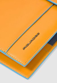 Oranje leren portemonnee met blauwe accenten, voorzien van gestikte randen en een metalen "Piquadro" logo. Compact ontwerp met meerdere kaarthouders.
