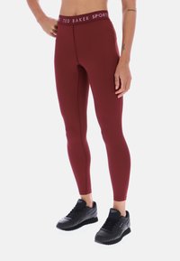Bordowe legginsy z wysokim pasem z logo "TED BAKER SPORT". Wykonane z elastycznego materiału, dopasowany krój, w parze z czarnymi butami sportowymi.