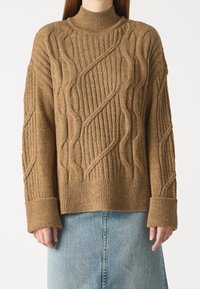 Ruskea neulottu villapaita, jossa on korkea kaulus, tekstuurillisia palmikkokuvioita, joustavat hihansuut ja rento istuvuus, yhdistettynä farkkuhameeseen.