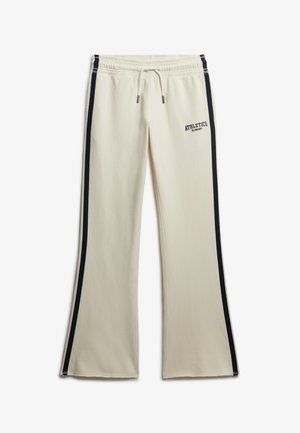 Pantaloni della tuta color crema con strisce laterali nere, una vita con cordino e la scritta "ATHLETICS" stampata sul davanti con lettering scuro.