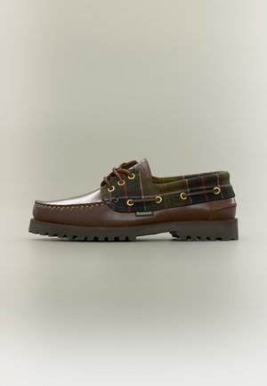 Chaussure bateau en cuir marron à carreaux verts avec semelle noire épaisse et laçage à l'avant, avec une étiquette de la marque Barbour sur le côté.