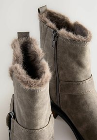 Graue Wildleder-Ankle Boots mit Futter aus Kunstfell, flachem Absatz, seitlichem Reißverschluss und Riemenbeschläge in der Nähe des Knöchels. Glatte Textur und abgerundete Form.