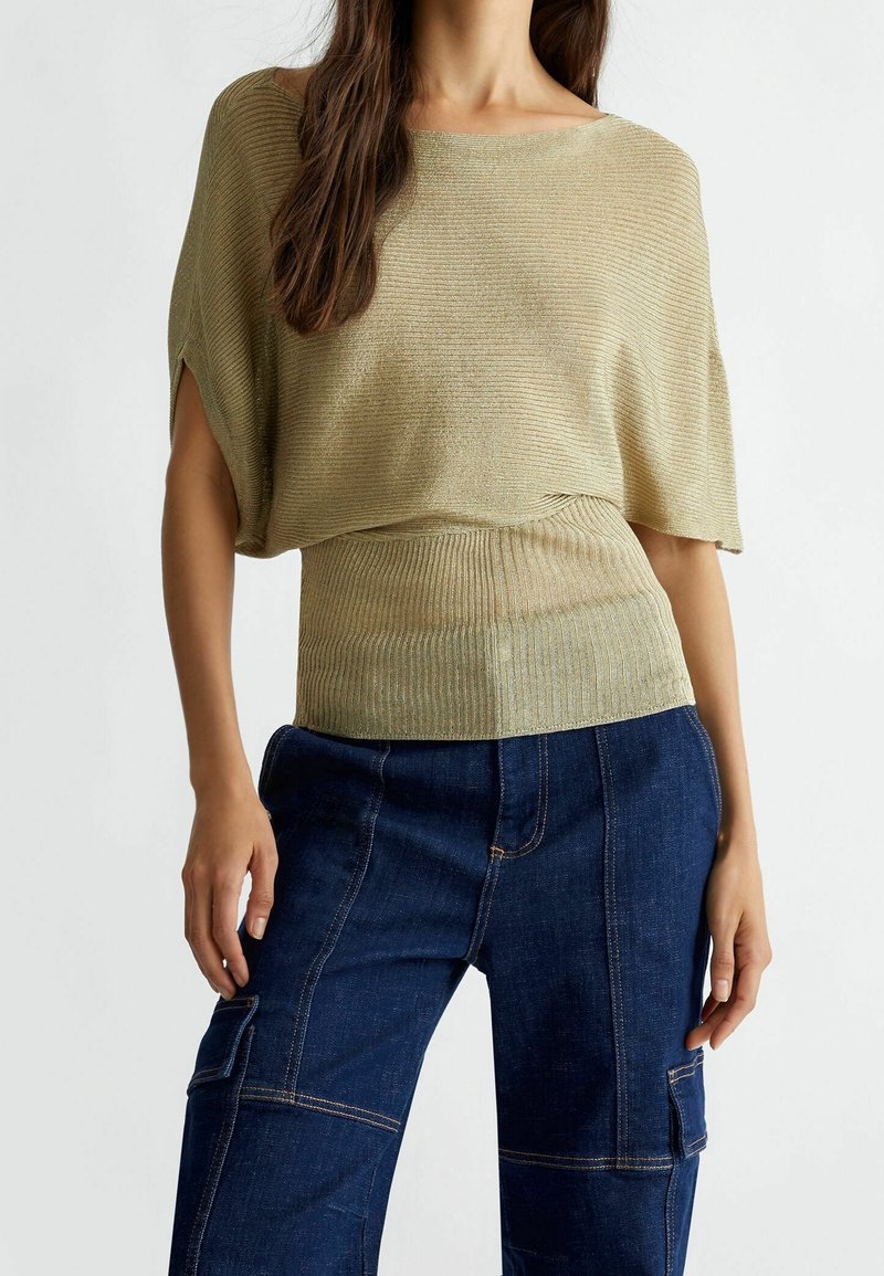Femme portant un haut beige côtelé ample à manches courtes et un jean cargo bleu foncé avec des coutures et des poches visibles.