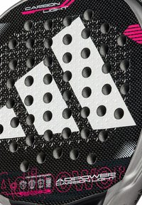 Padel racket met een zwarte carbonoppervlak, drie witte diamantvormen en ronde gaatjespatronen, met roze accenten en merkdetails.